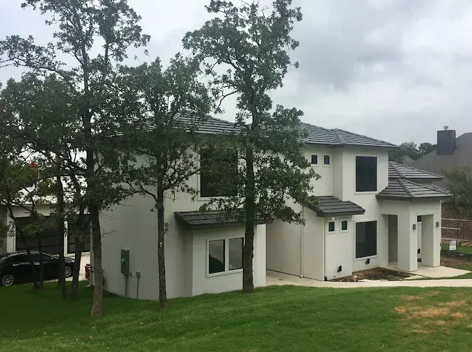 Modern two-story white house with dark gray roof and black window frames, trees in front, car in the driveway.