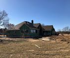 A one-story house under construction with green siding and a brown roof against a clear blue sky.