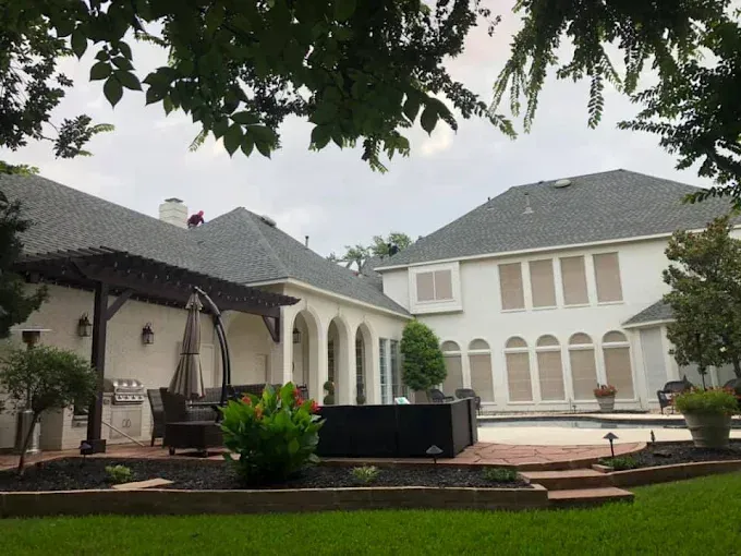 Luxury home exterior with pool and pergola, gray roofs, white walls, cloudy day.