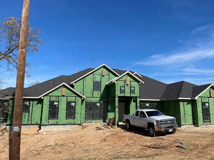 New house under construction with green exterior, black roof, and a white pickup truck parked in front.
