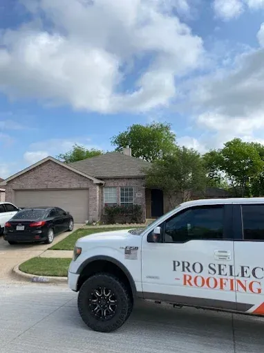White Pro Select Roofing truck in front of a brick house with a dark roof on a sunny day.