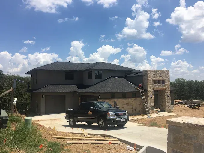 New two-story house under construction with gray siding, stone accents, black roof. A truck is parked in the driveway.
