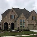 Brick house with dark roof and brown shutters under cloudy sky. Garage to the right.