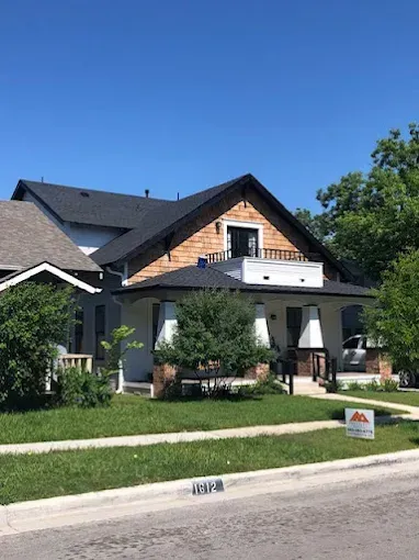 A two-story house with a porch. It has a cedar shingle gable, white siding, and a new black roof.