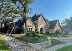 Stone house with multiple rooflines, lawn, landscaping, and a small creek.
