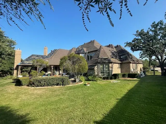 Large, multi-story home with a brown roof and brick exterior, viewed from a grassy yard on a sunny day.