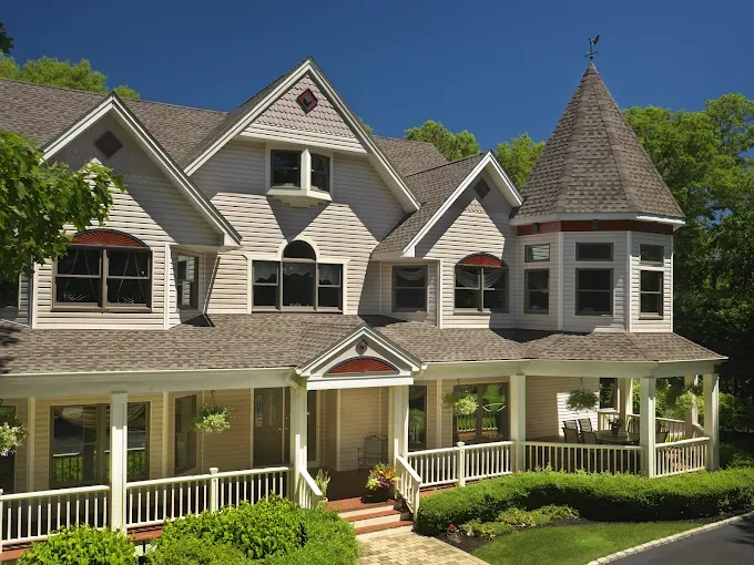 Victorian-style house with light siding, a porch, and a turret on a sunny day.