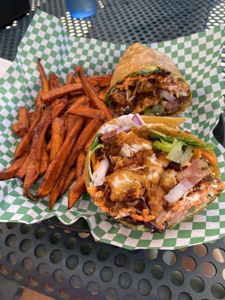 A chicken wrap cut in half served with a side of sweet potato fries on green and white checkered paper.