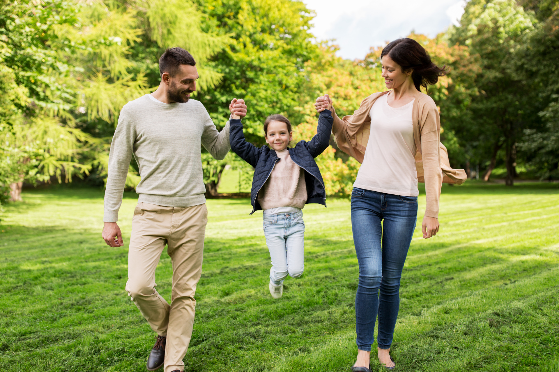 Family walking hand in hand through a green park, smiling on a sunny day
