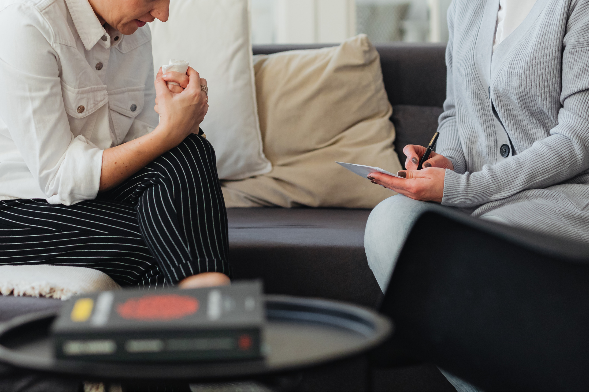Two people talking on a couch, one gesturing while the other holds a phone.