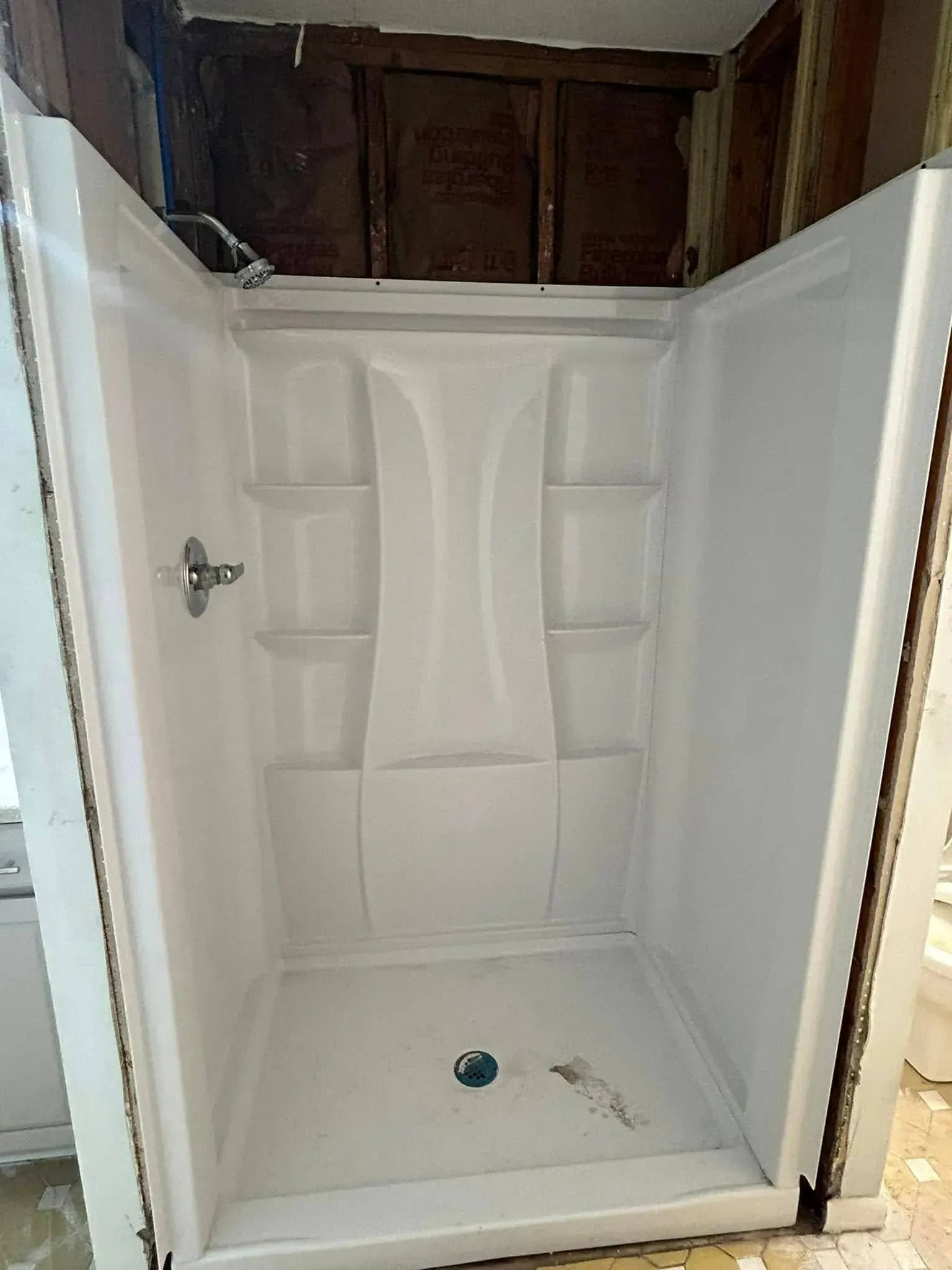 A white shower stall is being remodeled in a bathroom.
