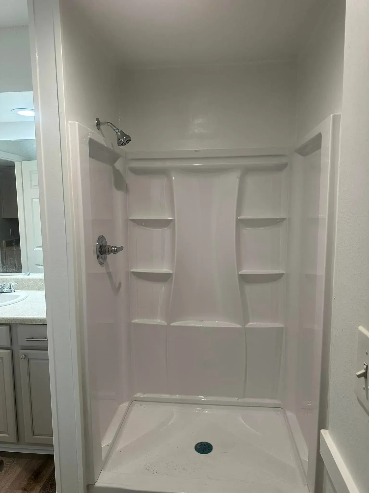 A white shower stall with shelves and a shower head in a bathroom.