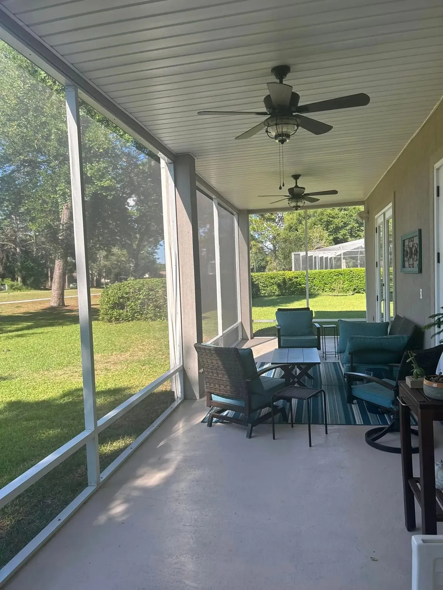 A screened in porch with a table and chairs and a ceiling fan.