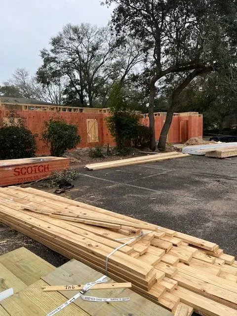 A pile of wood is sitting in front of a building under construction.
