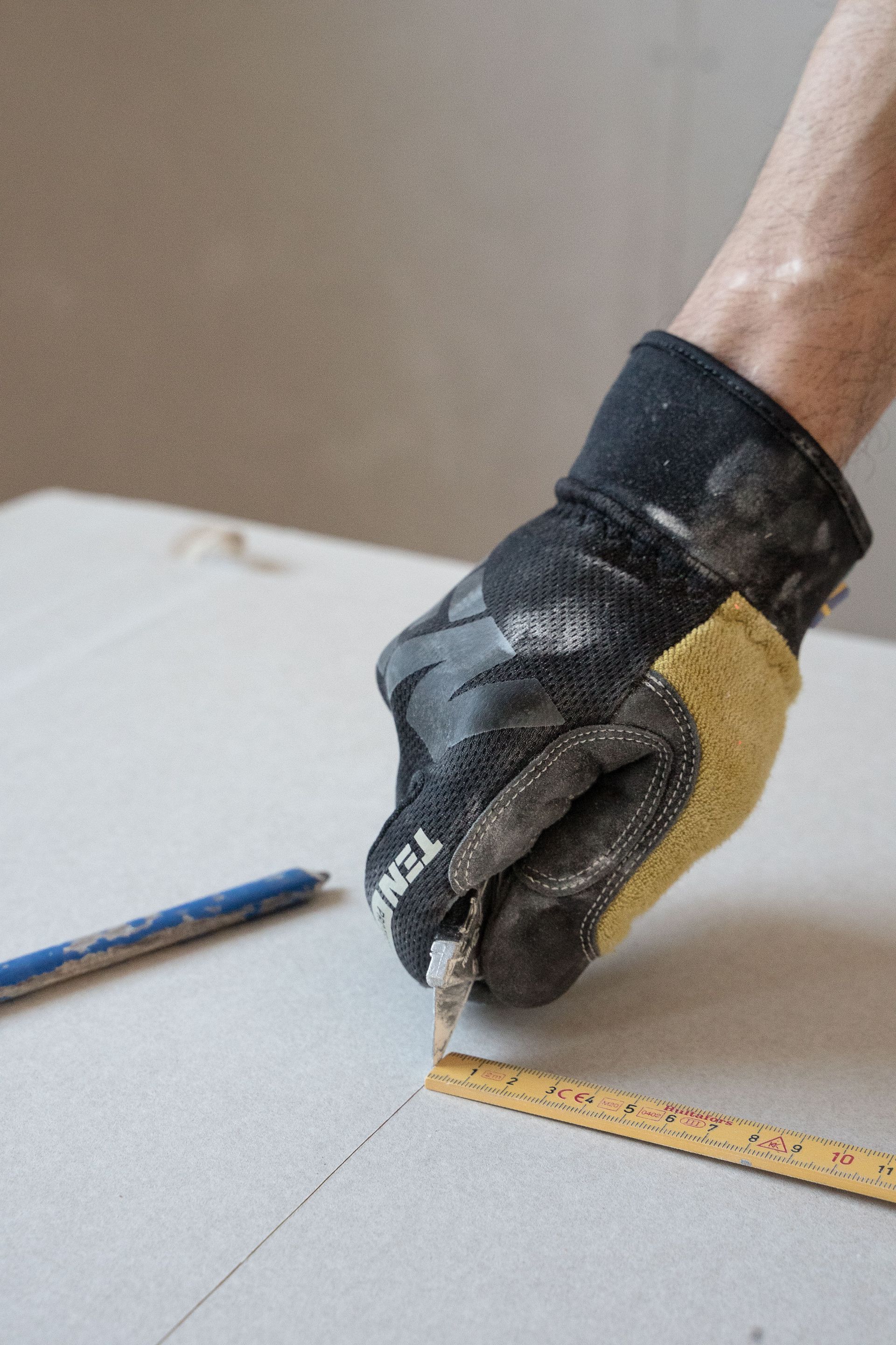 Gloved hand using a ruler and pencil to measure and mark a white surface
