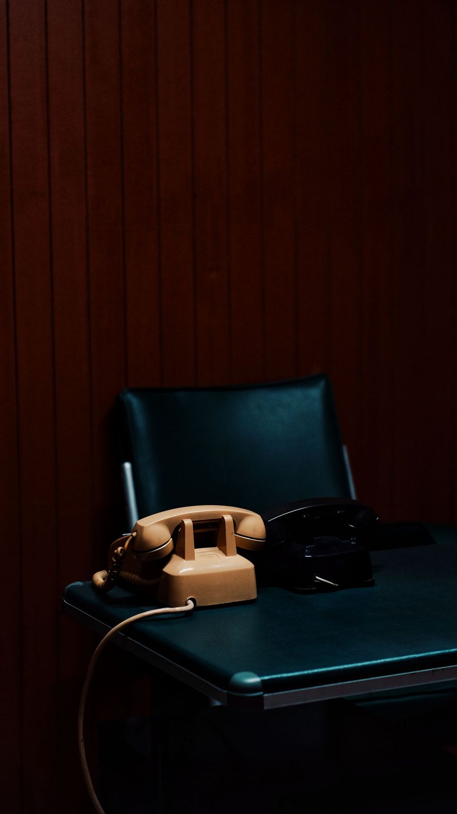 Vintage beige rotary phone on a dark chair against a wooden wall.