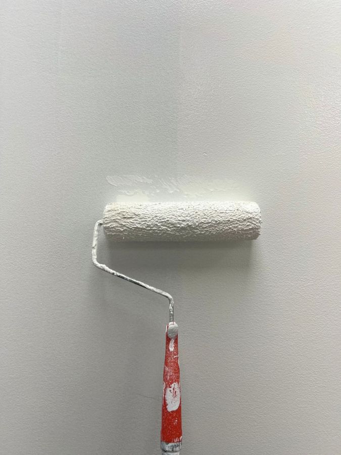 Paint roller with white paint against a light gray wall