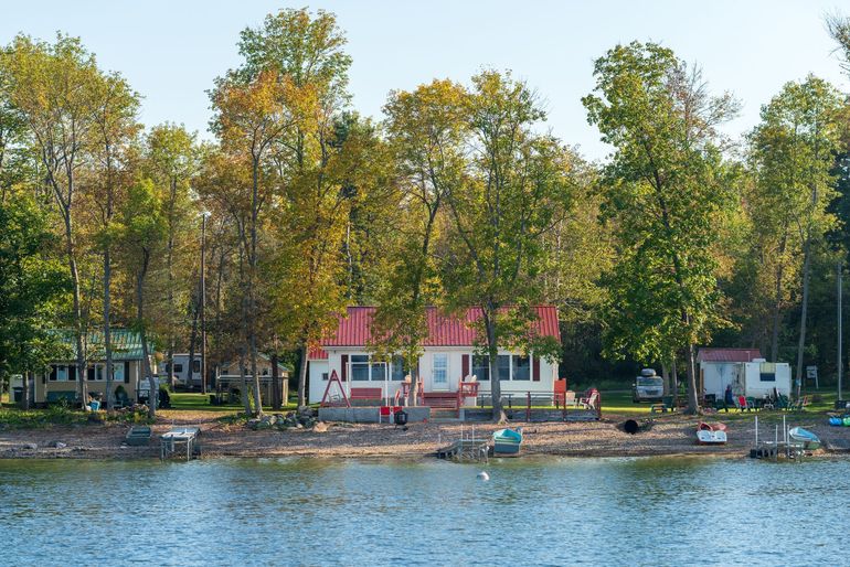 Riverside cottages with red roofs among trees, beside a calm waterfront and small boats