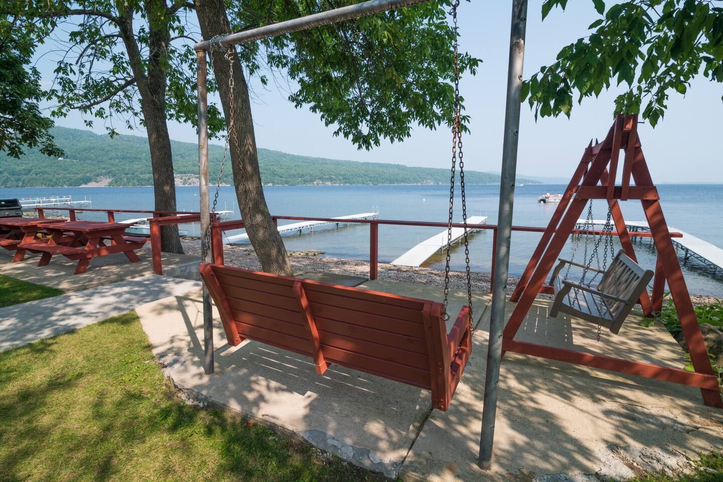 Lakeside picnic area with red wooden swing, benches, and a hammock under trees beside the water