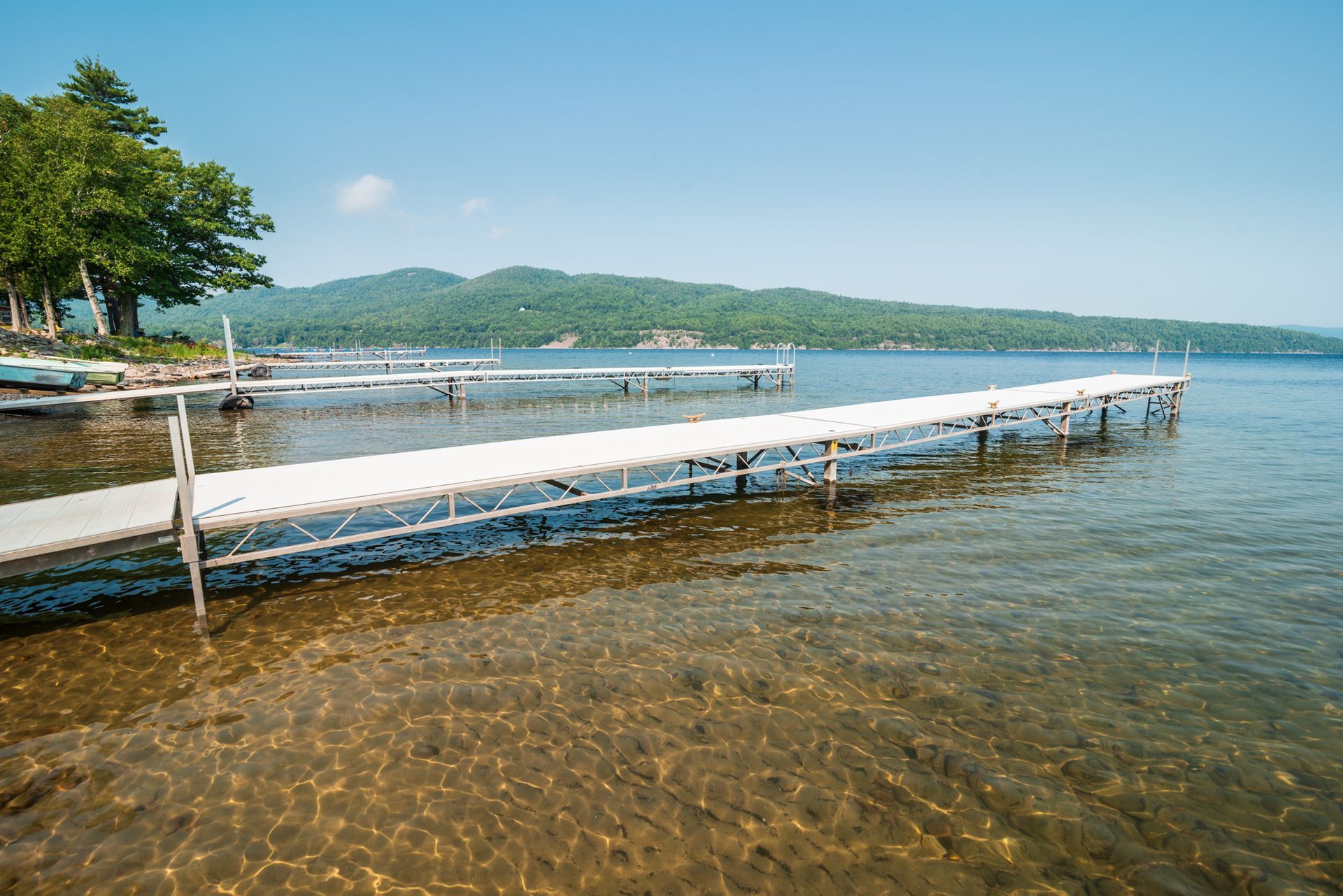 Floating dock on clear blue lake with a tree-lined shore and distant green hills