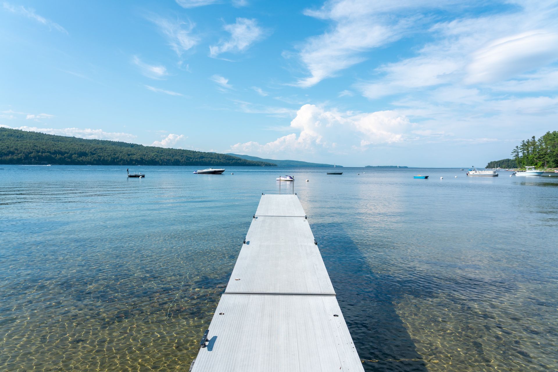 Wooden dock leading into a calm blue lake under a bright sky