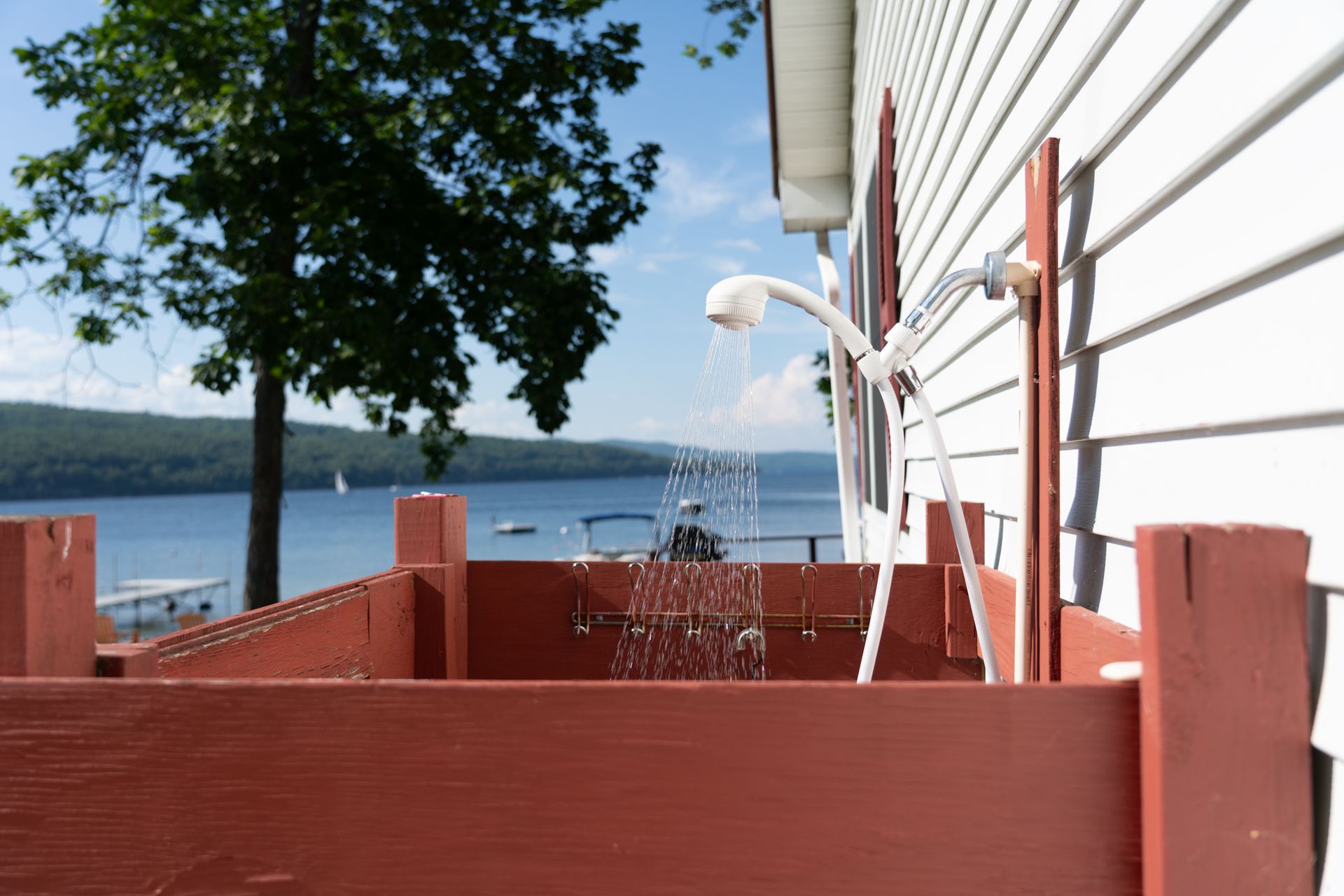 Red deck railing beside a white house, with a tree and lake view in the background.
