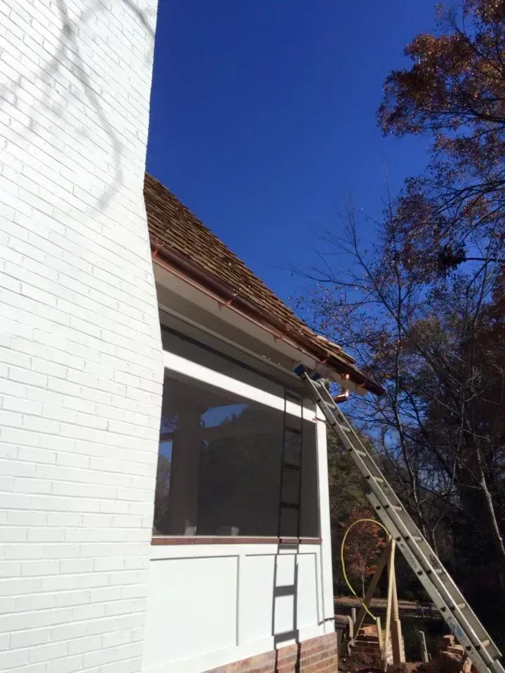 Exterior of white house with red-tiled roof, ladder leaning under blue sky and tree branches