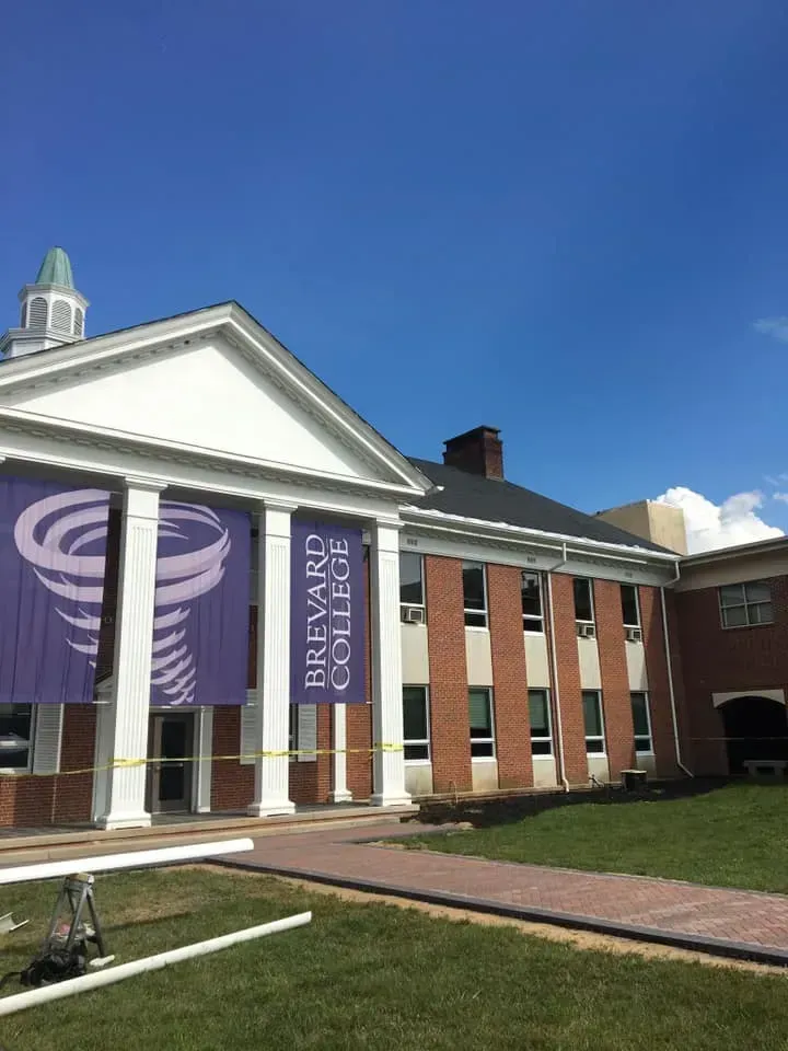 Brick academic building with white columns, purple banners, and a blue sky above a walkway.