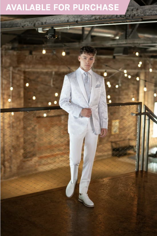 Man in a white suit standing on an indoor brick staircase with a “AVAILABLE FOR PURCHASE” banner.