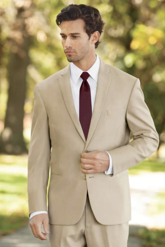 Man in a beige suit with a burgundy tie, standing outdoors and adjusting his jacket.