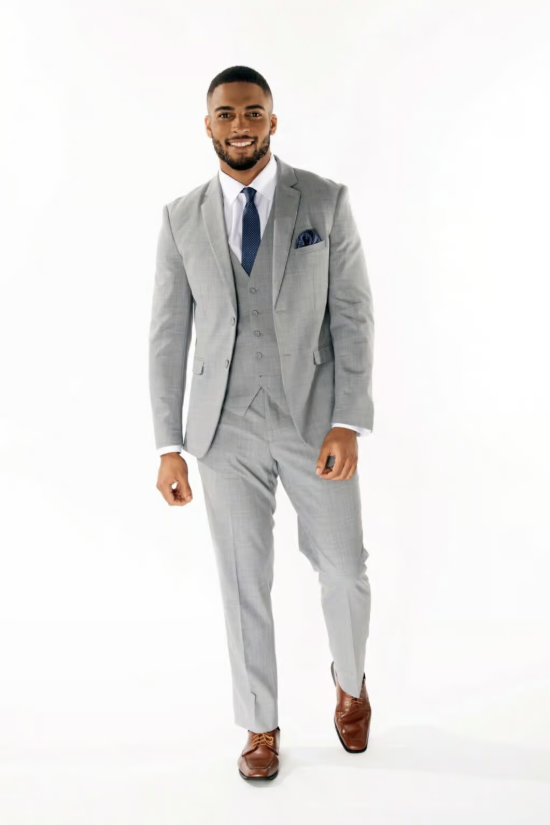 Man in a light gray suit walking toward camera on a white background