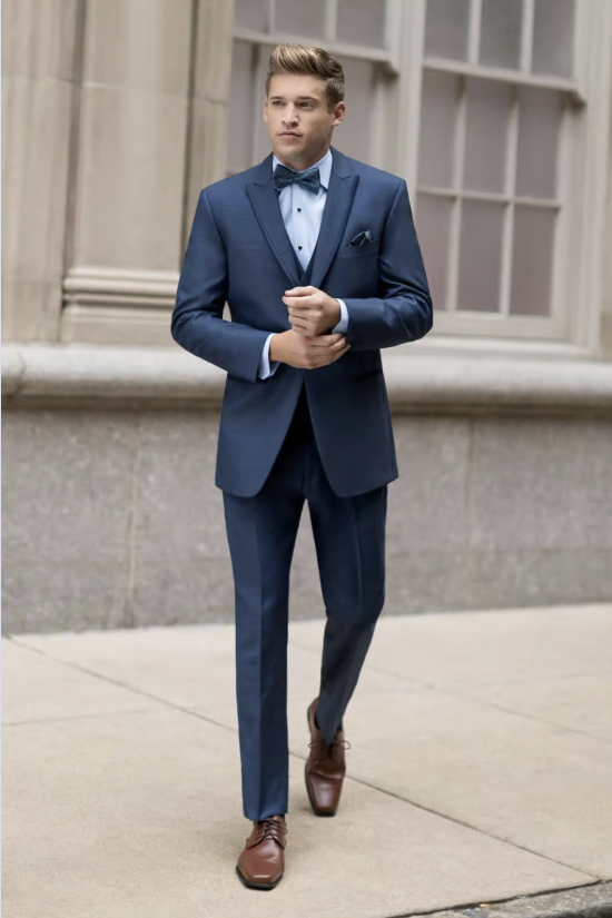 Man in a blue suit and bow tie walking on a sidewalk outside a building
