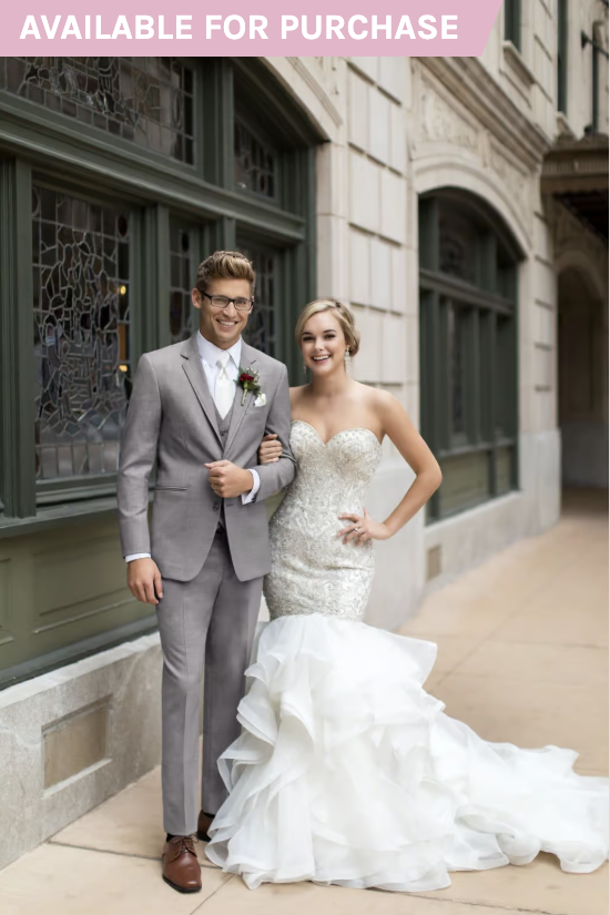 Bride and groom posing in wedding attire on a city sidewalk, with a storefront behind them.