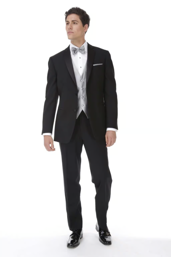 Man in a black tuxedo with a white vest and bow tie, standing against a white background.