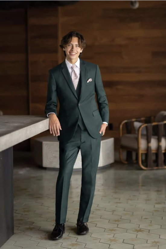 Man in a dark green suit standing in a modern wood-paneled room, leaning on a concrete bench.