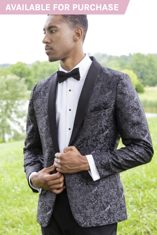 Man in a patterned black suit jacket and bow tie standing outdoors on grass