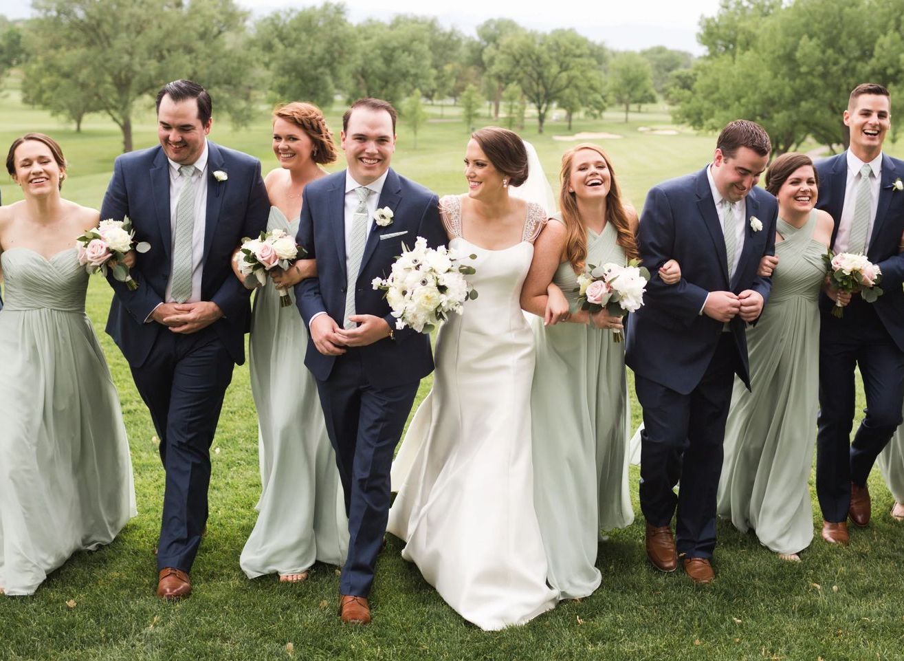 Wedding party walking outdoors on grass, carrying bouquets and smiling