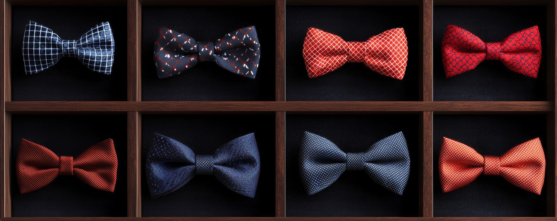 A display of eight bow ties in blue, red, and black arranged in a grid on a dark shelf.