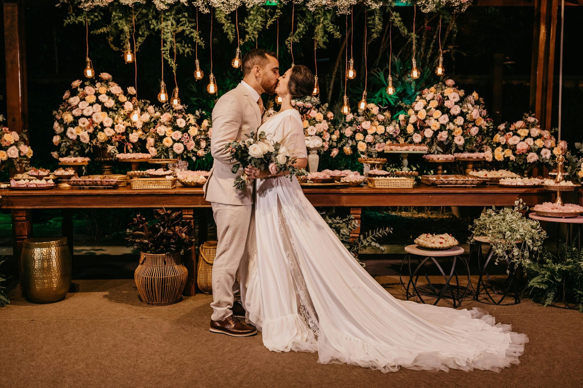 Bride and groom kissing before a floral wedding backdrop with warm lights