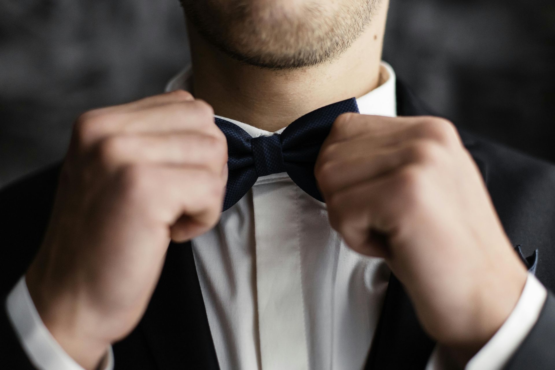 Man adjusting a black bow tie over a white dress shirt and black suit jacket