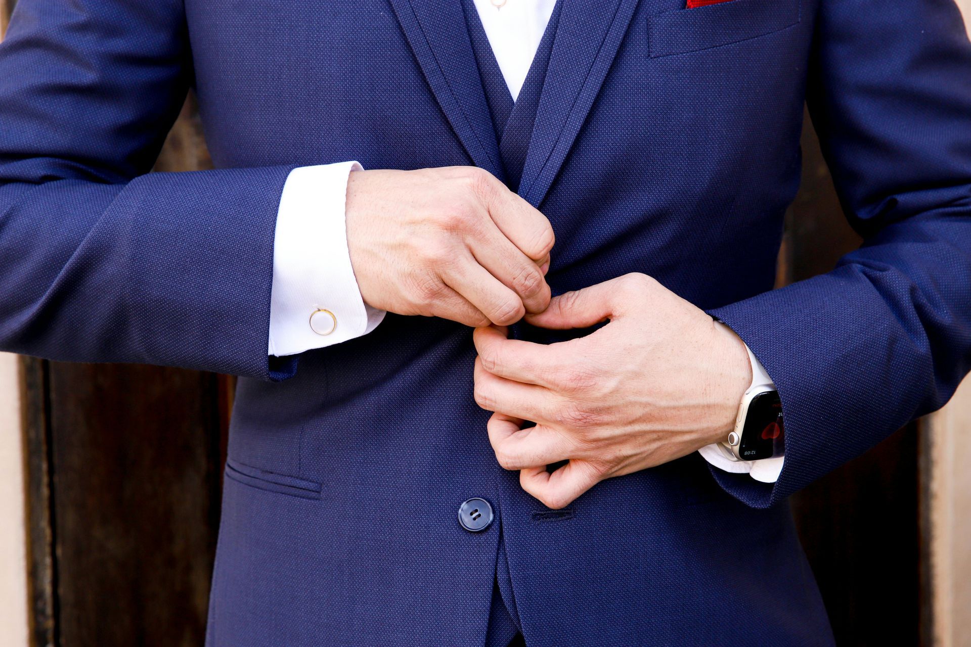 Close-up of a person buttoning a blue suit jacket with a white shirt and wristwatch visible