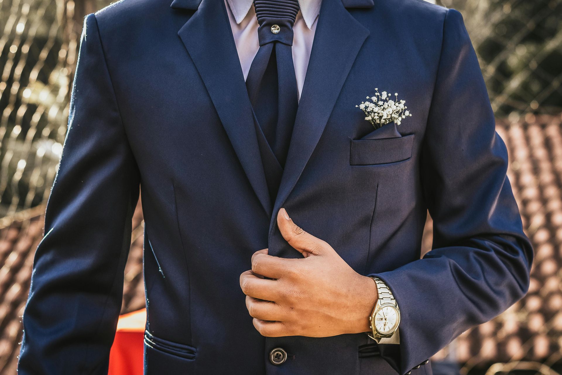Man in a navy suit adjusting his jacket, with a tie and pocket square, at a formal event.