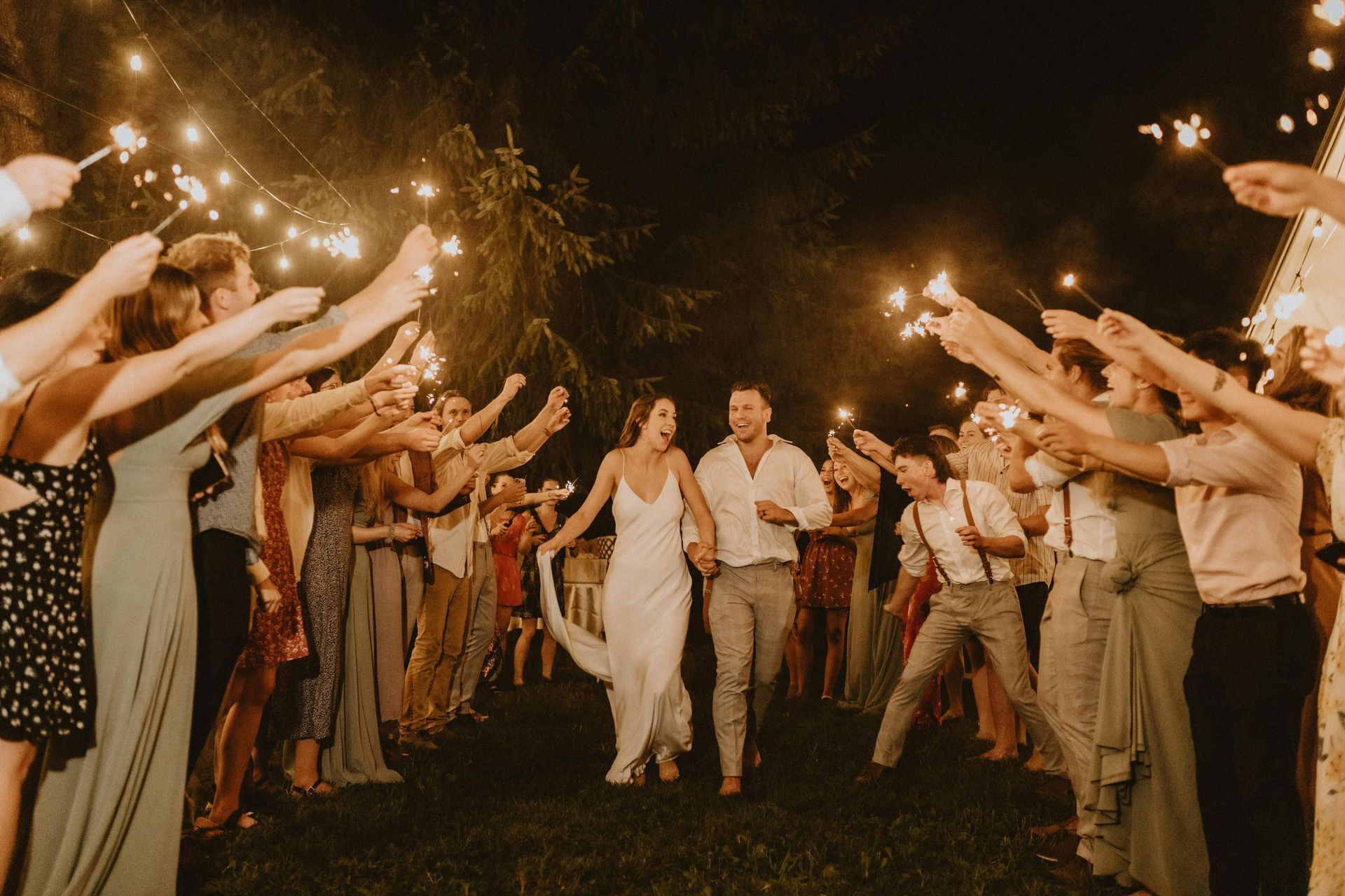 Couple walking through a sparkler tunnel as guests line both sides at an outdoor nighttime celebration
