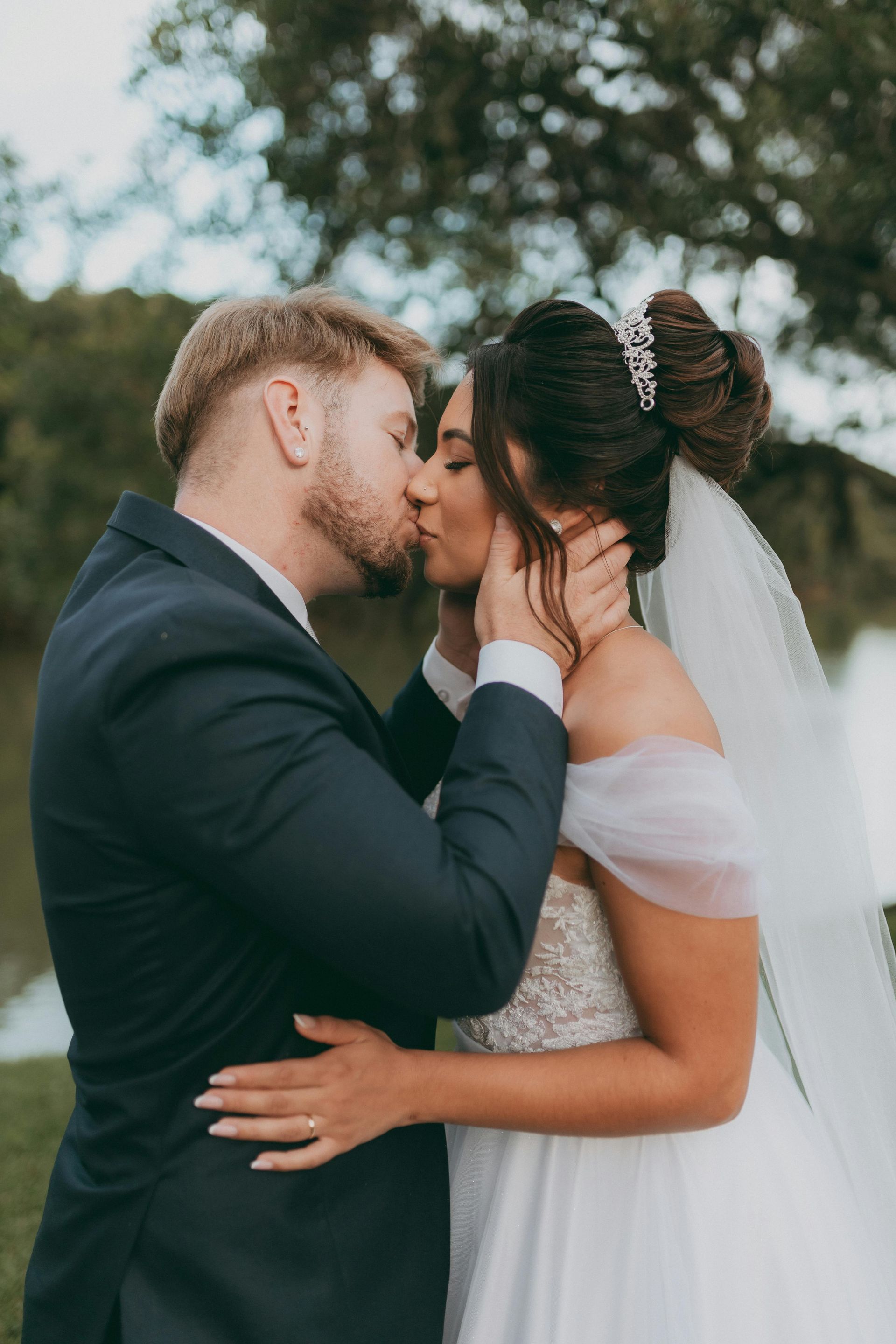 Bride and groom kissing outdoors, bride in white dress and veil, groom in dark suit