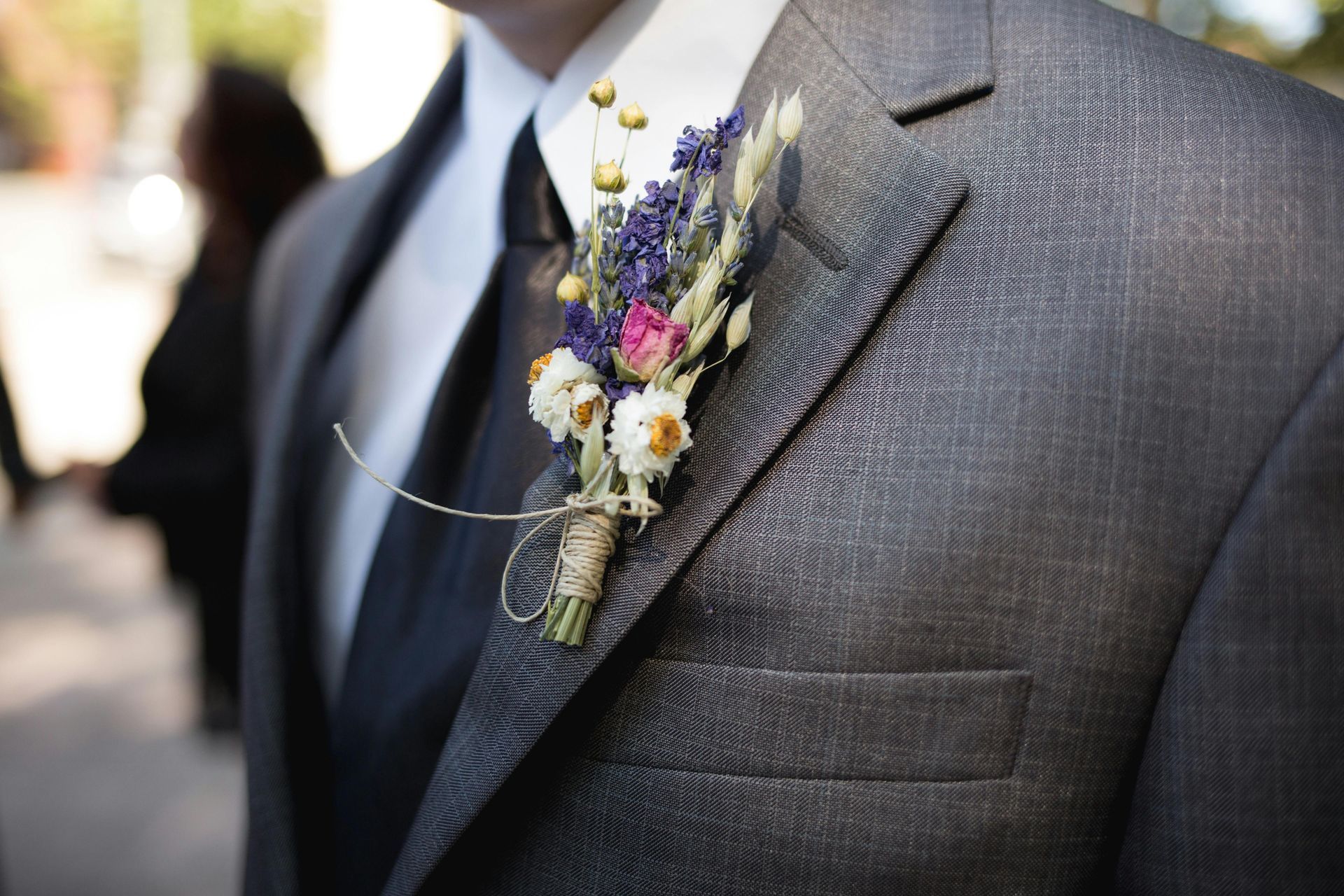 Gray suit jacket with a small purple and white boutonniere pinned to the lapel
