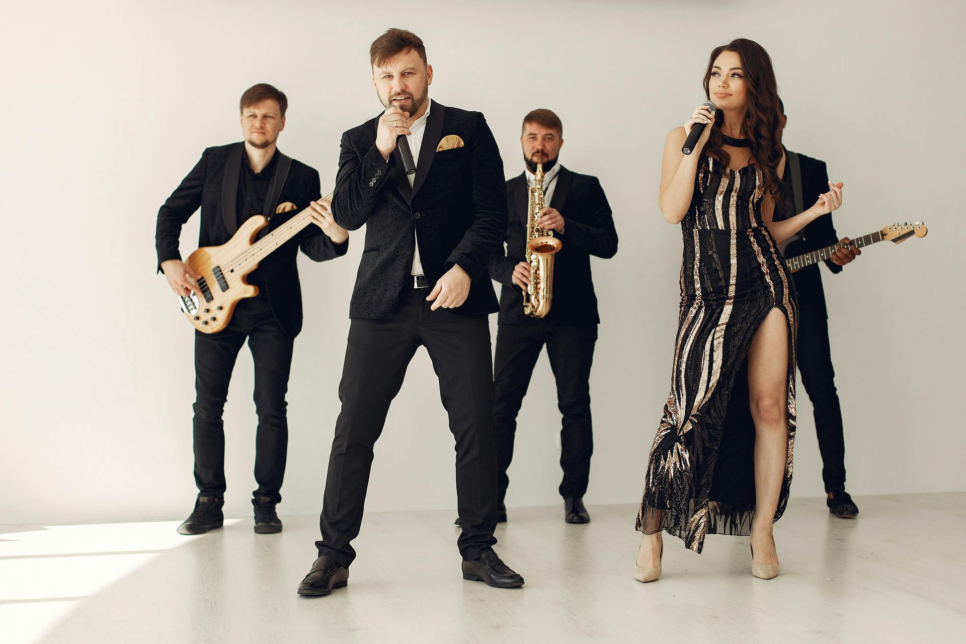 Four musicians performing in a studio, with microphones, guitars, and a saxophone against a white backdrop.