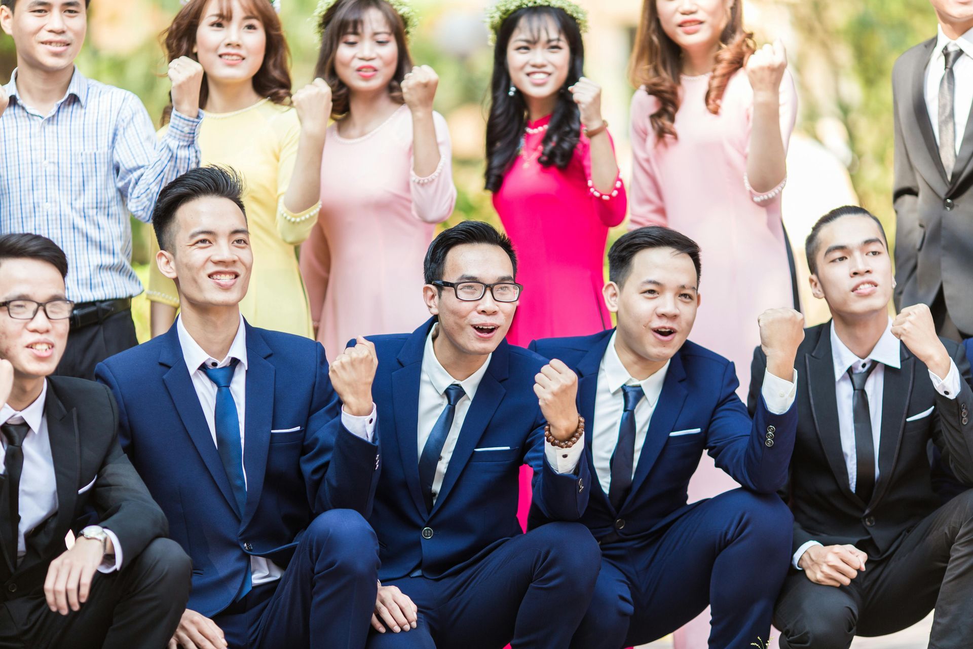 Group of people in formal attire posing and smiling outdoors, with several men seated in the front row.