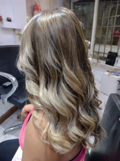 Una mano enguantada tiñe el cabello con un pincel junto a un recipiente con tinte azul y rojo.