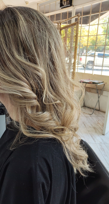 Persona con abrigo gris y cabello rojo rizado de pie al aire libre cerca de un seto.