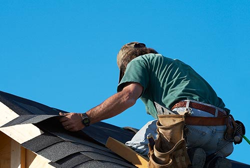 A man is working on a roof with a blue sky in the background.
